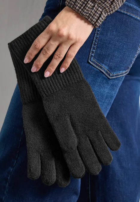 Zwarte, gebreide vingerhandschoenen, vastgehouden door een hand voor een spijkerbroek.