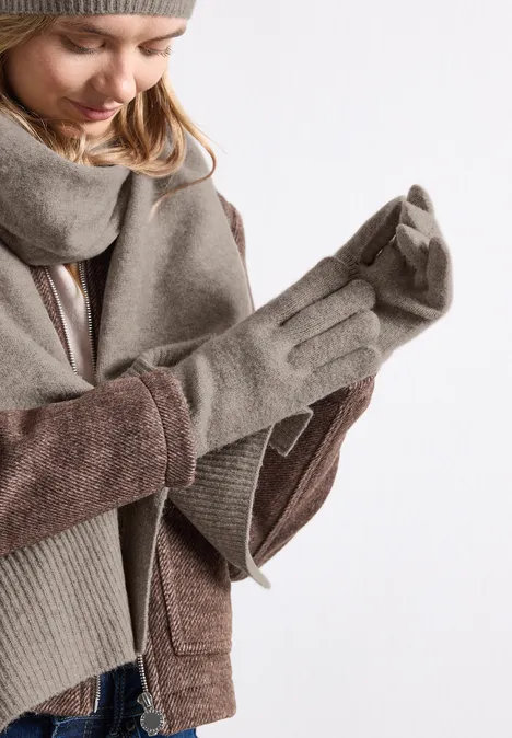 Feinstrick Handschuhe in Unifarbe Sandy Mocca Mel. Frau in Winterbekleidung zieht graue Handschuhe an.