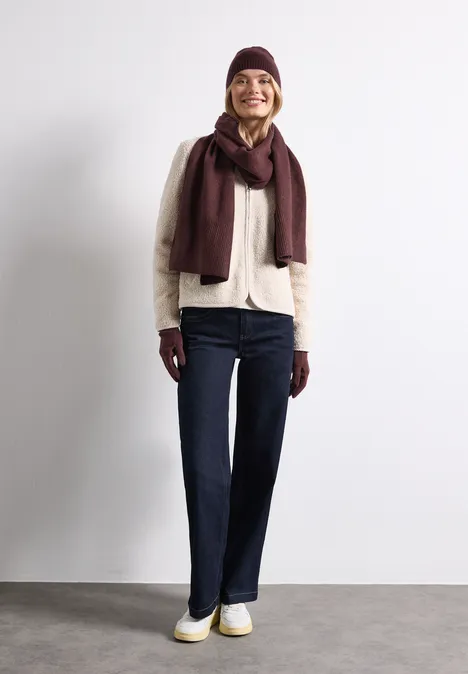 Feinstrick Handschuhe in Unifarbe rustic rouge mel. Eine Frau in einem neutralen Cardigan, dunklen Jeans, burgunderrotem Schal und Mütze posiert vor weißer Wand.