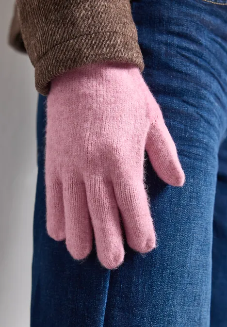 Close-up van een persoon met een roze fleecahandschoen naast een spijkerbroek en een bruine jas.