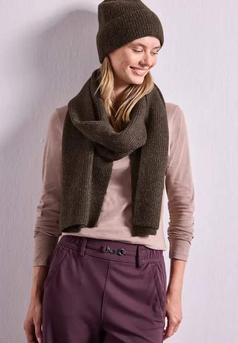 Schal im Melange-Look auburn brown mel. Junge Frau mit brauner Mütze, Wollschal, beiger Bluse und violetter Hose vor hellem Hintergrund.