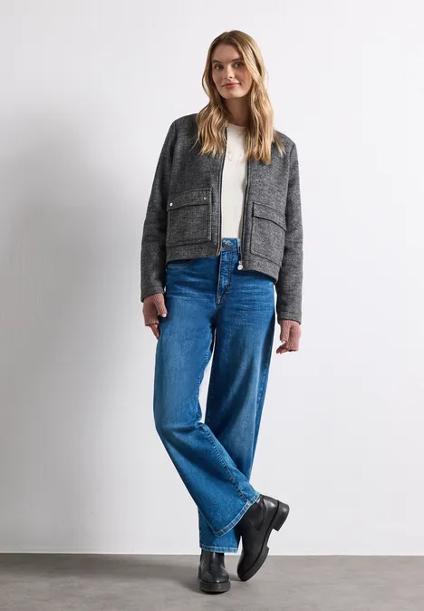 Armwärmer im Melange-Look vintage blush mel. Junge Frau steht vor weißem Hintergrund, trägt graues Sakko, weißes Shirt und weite blaue Jeans.