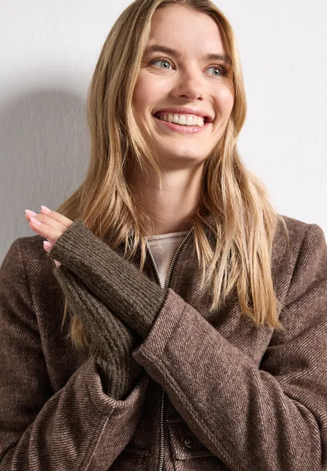 Armwärmer im Melange-Look auburn brown mel. Eine lächelnde Frau in braunem Mantel und fingerlosen Handschuhen vor hellem Hintergrund.