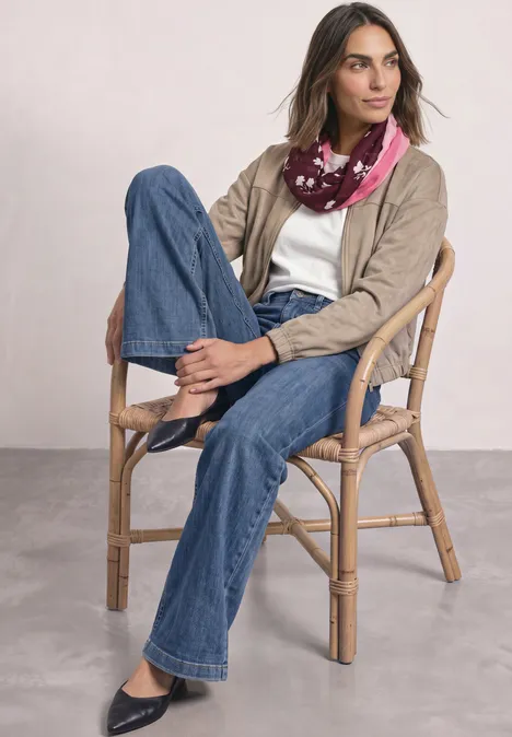 Loop-sjaal met bloemmotief rustic rouge Vrouw zit ontspannen op een rotan stoel, draagt wijde jeans, wit T-shirt, beige jasje en kleurrijke sjaal.