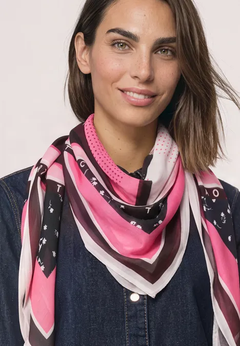 Foulard carré à imprimé graphique multicolor Porträt einer Frau mit braunen Haaren, die ein pink-weiß-schwarzes Tuch um den Hals trägt.