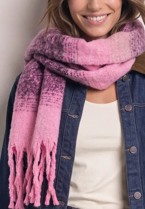 Frau trägt lächelnd einen rosa Farbverlauf-Schal mit Fransen über Jeansjacke und weißem Oberteil.