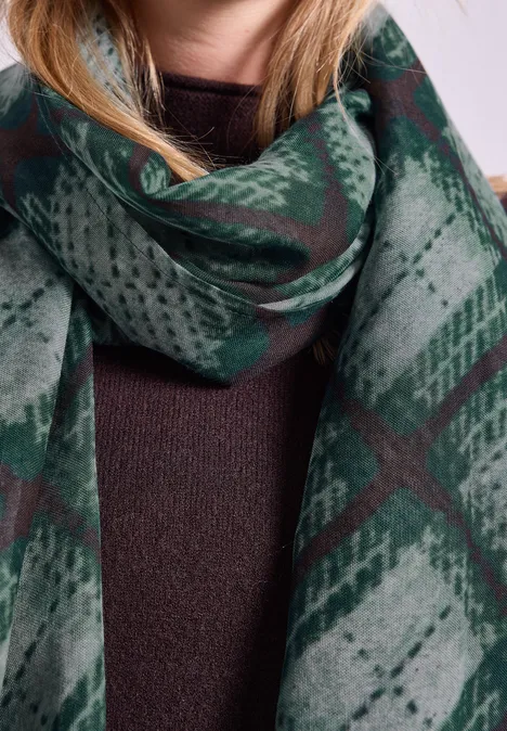 Een vrouw draagt een groene, geruite sjaal op een bruin truitje.