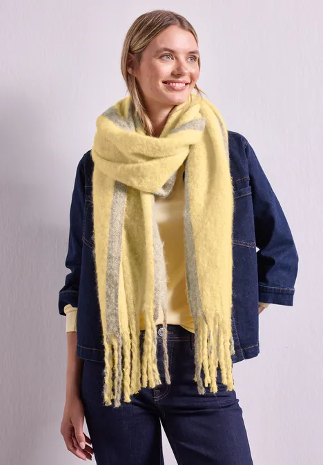 Langer Schal im Two-Tone-Look sunbeam yellow Frau mit gelbem, flauschigem Schal, Jeansjacke, lächelt seitlich vor hellem Hintergrund.