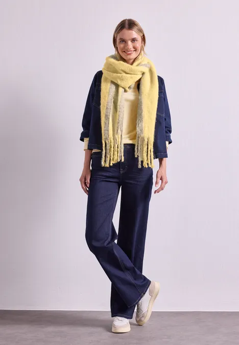 Langer Schal im Two-Tone-Look sunbeam yellow Frau in dunkelblauer Jeanshose und Jacke, trägt einen großen, gelben Schal und weiße Sneaker.