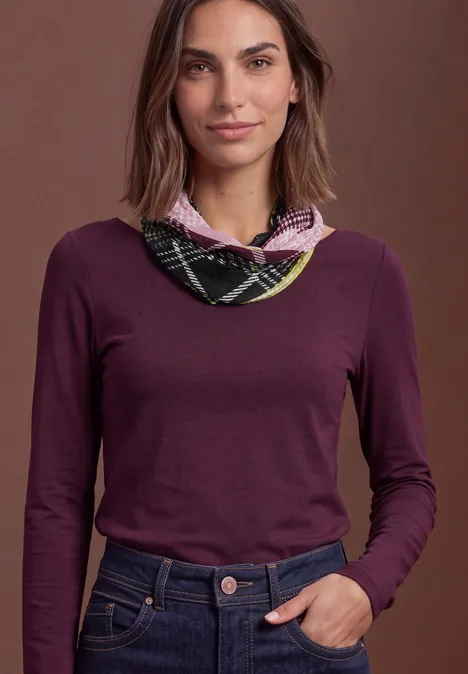 Loop-Schal mit Karomuster multicolor Frau im violetten Langarmshirt und kariertem Halstuch vor braunem Hintergrund, Hand locker in der Jeanshose