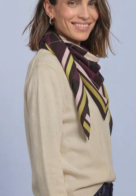 Zijaanzicht van een vrouw in een beige trui met een gestreept sjaaltje om haar hals.