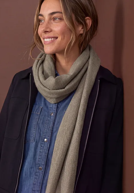 Frau mit schwarzem Mantel, blauem Jeanshemd und beigem Schal lächelt zur Seite.