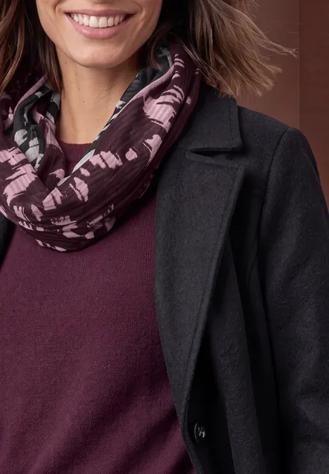 Loop-Schal mit Struktur und Print Black Teilansicht einer lächelnden Frau in dunkelgrauem Mantel, burgunderfarbenem Pullover und gemustertem Loop-Schal.