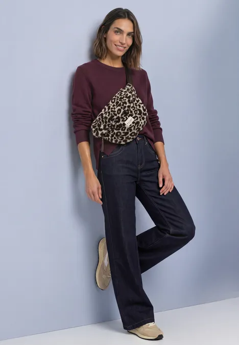 Teddy-Umhängetasche mit Leo-Muster auburn brown Frau in lila Pullover mit Leopardenmuster-Tasche, weitem Jeans und beigen Schuhen vor hellblauem Hintergrund.