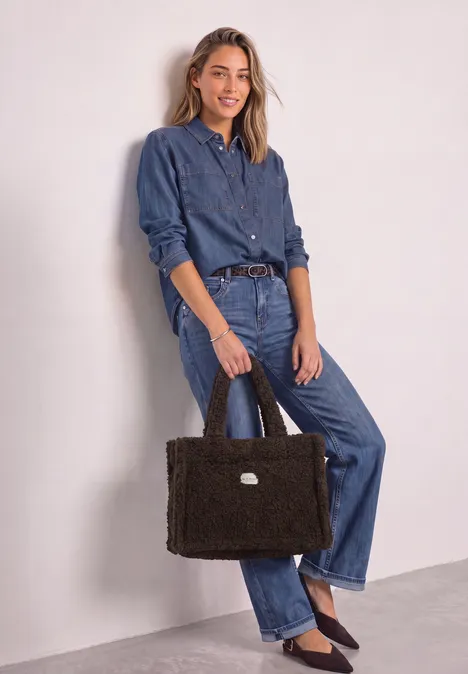 Sac de transport pour peluche, couleur unie auburn brown Frau in Jeanshemd und Jeanshose mit schwarzer, flauschiger Tasche vor hellem Hintergrund.