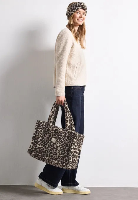 Slanke vrouw met panterpet, beige trui, wijde jeans en gele schoenen draagt een panterprint tas.