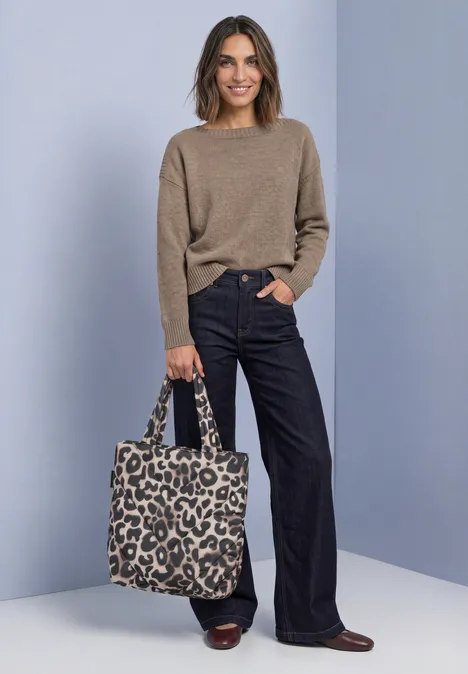 Sac cabas doublé à motif léopard multicolor Frau in beigem Pullover und weitem blauen Jeans, braunen Schuhen, trägt eine Leo-Tasche vor schlichtem Hintergrund