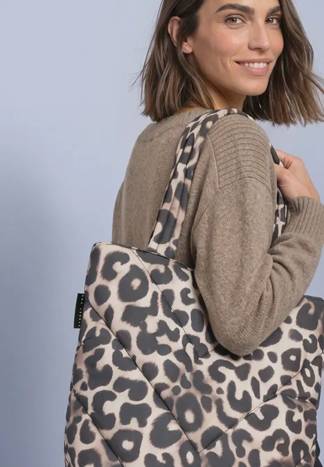 Sac cabas doublé à motif léopard multicolor Frau in beigem Pullover lächelt und trägt eine Tragetasche mit Leopardenmuster über der Schulter.