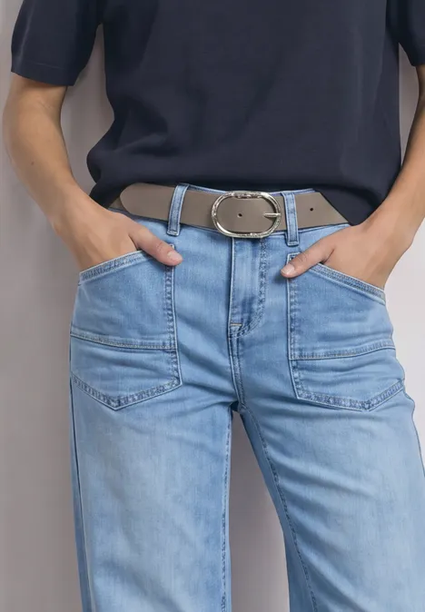 Riem met decoratieve gesp Muddy Mocha Person mit blauer Jeans, breitem Gürtel und dunklem Oberteil, Hände in den Taschen