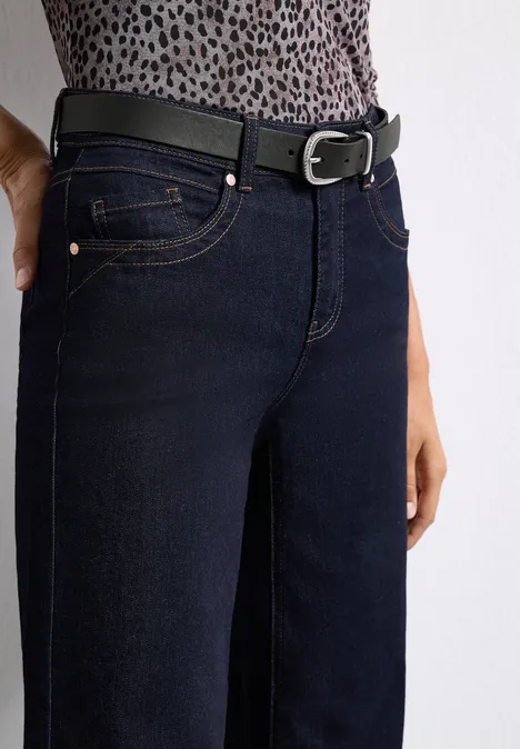 Basic riem met gesp Black Dunkelblaue Jeans mit schmaler Passform, kombiniert mit einem schwarzen Gürtel vor weißem Hintergrund.