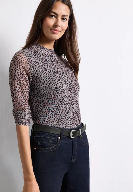 Basic riem met gesp Black Frau in semi-transparentem Leopardenmuster-Shirt und dunkler Jeans vor weißem Hintergrund.