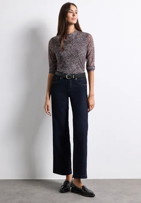 Basic riem met gesp Black Frau in gemustertem Oberteil und weiten, dunklen Cropped-Hosen, schwarze Loafer.