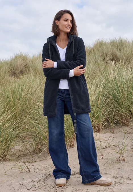 Strukturmix Teddy-Mantel mit Kapuze dark navy blue Frau in lockerer Jeans und Cardigan steht entspannt in Dünen und lächelt.