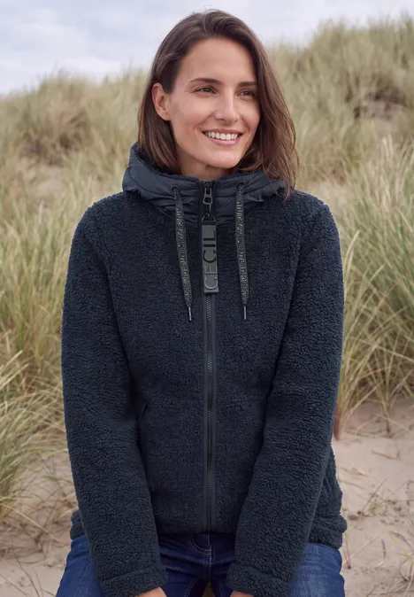 Strukturmix Teddy-Mantel mit Kapuze dark navy blue Lächelnde Frau im dunklen Fleece-Hoodie vor Strandgras