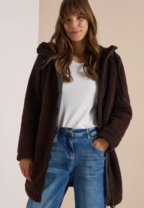 Strukturmix Teddy-Mantel mit Kapuze chocolate sauce brown Frau in braunem Teddy-Mantel mit Kapuze über weißem T-Shirt und Jeans, lächelt leicht.