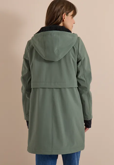 Une personne de dos porte un parka vert à capuche, longueur genoux.