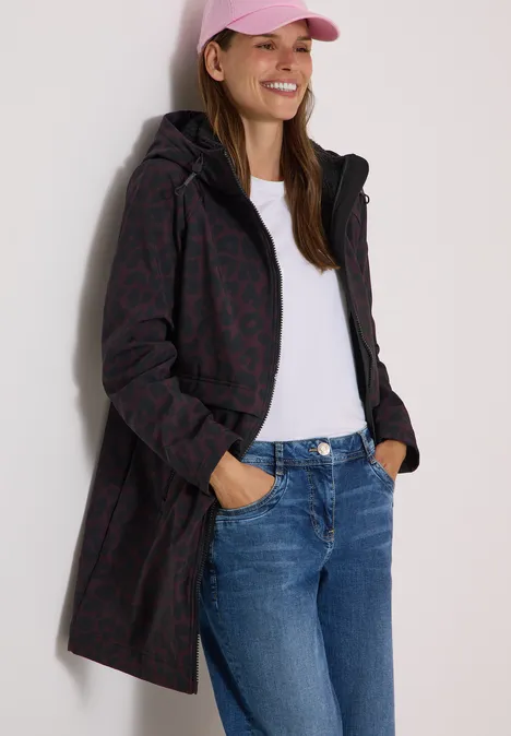 Femme en jean, T-shirt blanc et long manteau à capuche à motif, portant une casquette rose.