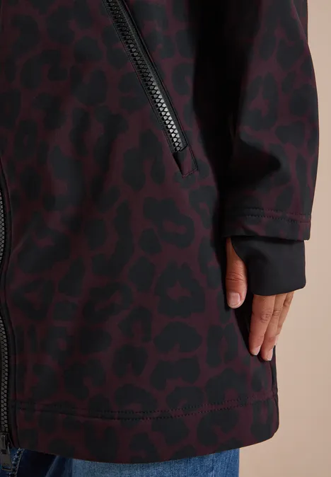 Gros plan d'un manteau bordeaux à motif léopard noir, poche zippée latérale et main visible.