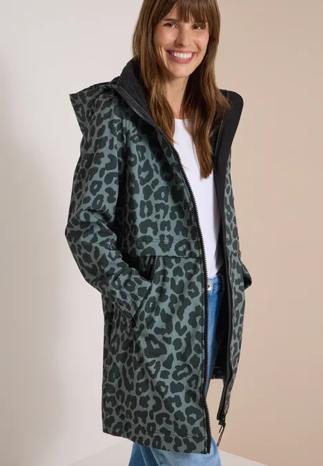 Femme souriante portant un manteau vert à capuche avec imprimé léopard noir.