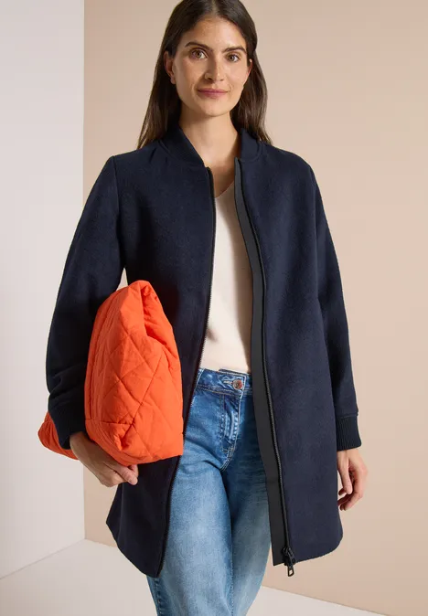 Langer Blouson mit Wollanteil dark navy blue Modische Frau trägt marineblauen Mantel, weißes Top, Jeans und hält eine orangefarbene Tasche unter dem Arm.