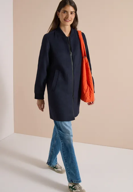 Langer Blouson mit Wollanteil dark navy blue Eine Frau in einem dunklen Mantel, blauen Jeans und roter Tasche steht vor hellem Hintergrund.