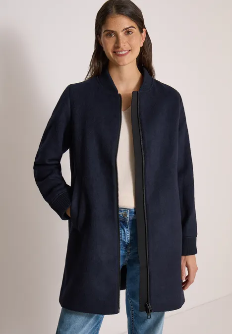 Langer Blouson mit Wollanteil dark navy blue Frau in dunkelblauem Mantel mit Reißverschluss und Taschen, dazu Jeans und weißer Pullover.