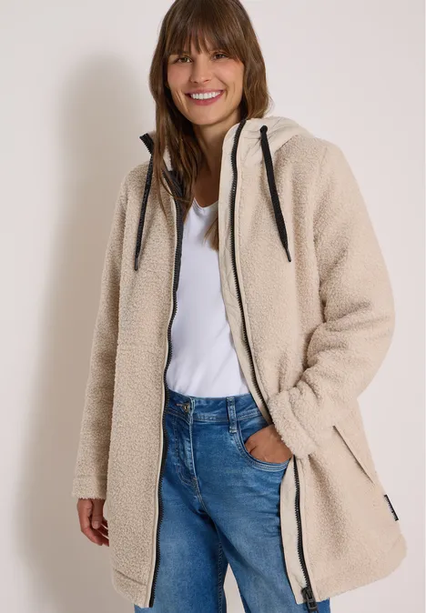 Strukturmix Teddy-Mantel mit Kapuze teddy vanilla white Frau in beigem Teddy-Fleece-Mantel mit Kapuze, Jeans und weißem Shirt, lächelt in die Kamera.