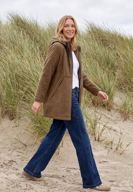 Eine Frau spaziert fröhlich am Strand vor Sanddünen.