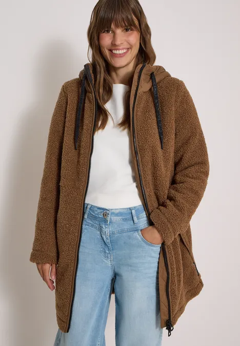 Strukturmix Teddy-Mantel mit Kapuze dark toffee brown Frau in braunem Teddy-Mantel, weißem Shirt und blauer Jeans, entspannt lächelnd.
