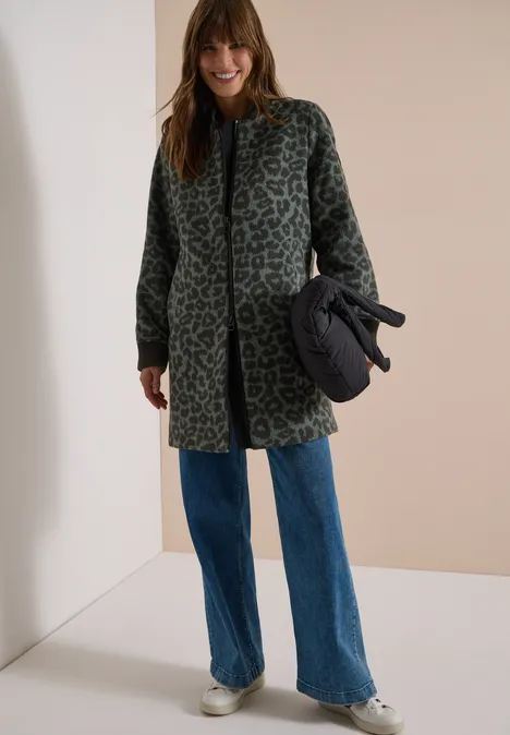 Langer Blouson mit Wollanteil olive night Frau in grün-grauem Leo-Mantel, weiten Jeans und Sneakers, hält eine schwarze Tasche.