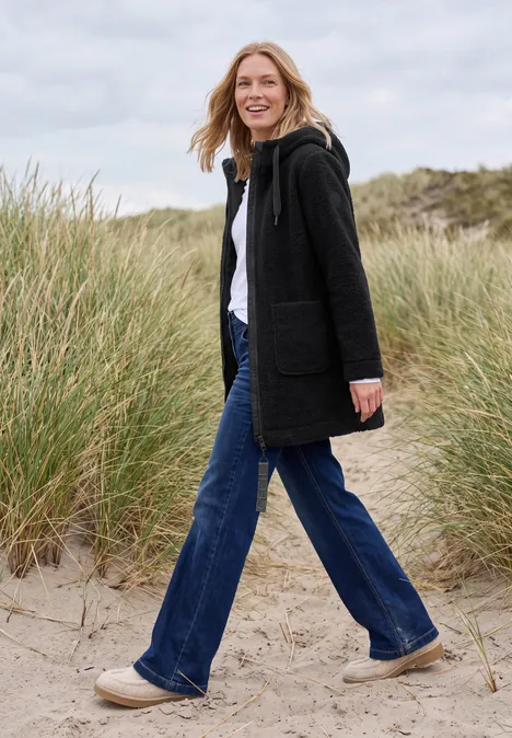 Mantel in angerauter Wolloptik Black Eine Frau spaziert am Strand durch Dünen, trägt schwarzen Mantel, Jeans und helle Schuhe.