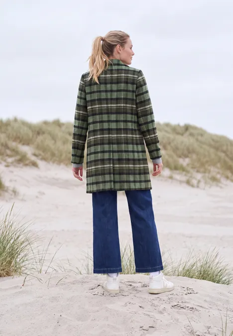 Frau von hinten in grün kariertem Mantel, blonder Pferdeschwanz, Jeans und weißen Sneakern auf Dünen.