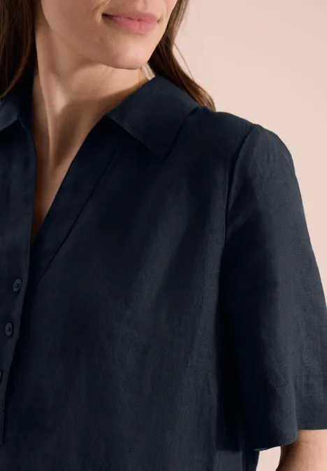 Een vrouw draagt een donkerblauw linnen overhemd met korte mouwen en kraag.