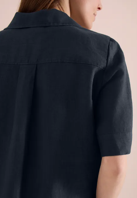 Achteraanzicht van een persoon met halflang bruin haar in een zwart linnen overhemd met korte mouwen.