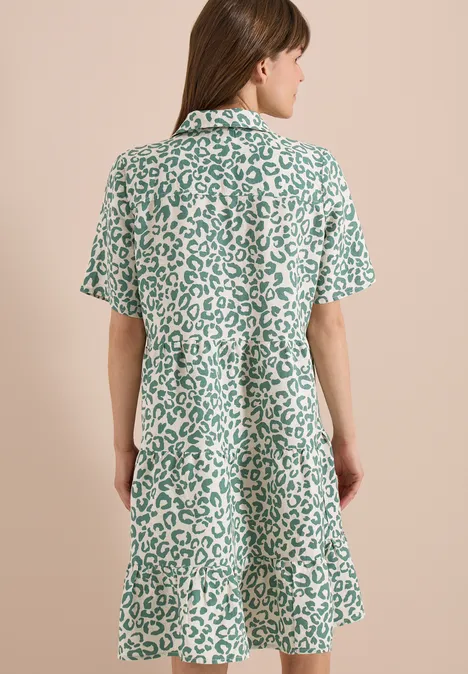 Rückenansicht einer Frau in lockerem, kurzärmligem Kleid mit grün-weißem Leopardenmuster.