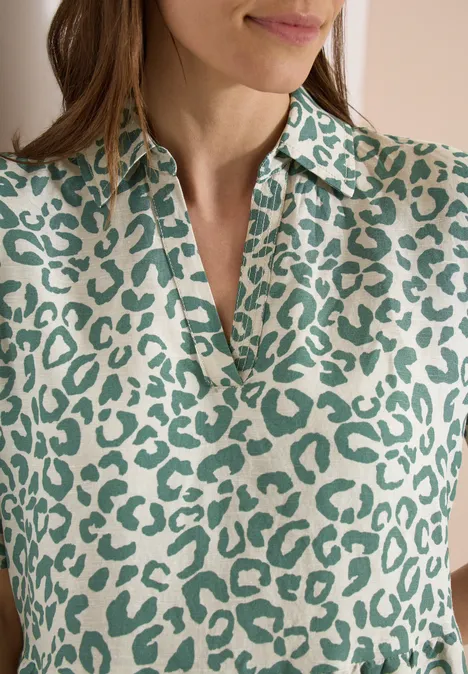 Frau in cremefarbenem Oberteil mit grünem Leopardenmuster.
