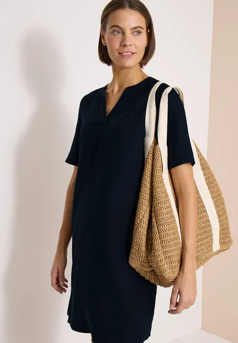 Vrouw in marineblauwe knie-lange jurk met V-hals en korte mouwen, met grote strozak over de schouder.