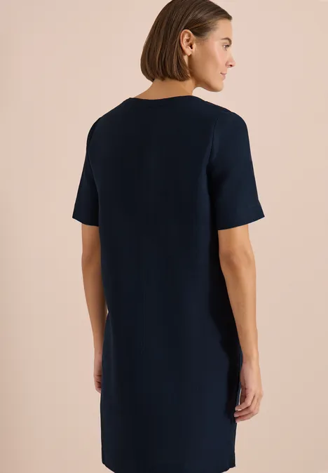 Vrouw van achteren in een eenvoudig, kort mouwig, marineblauw jurkje