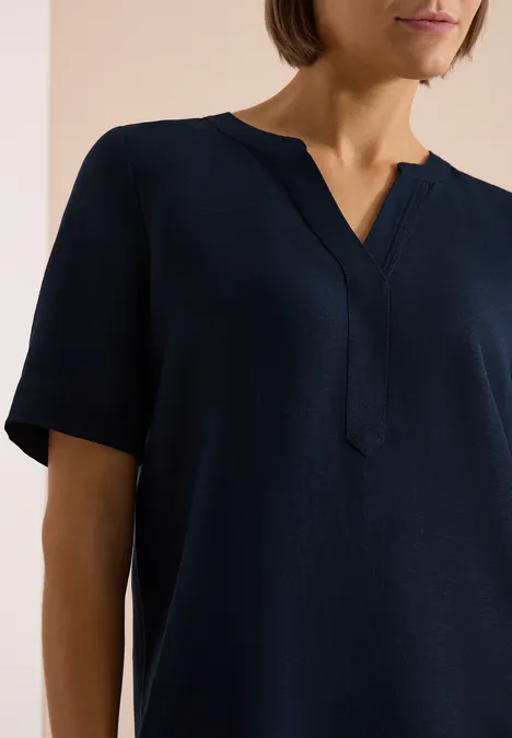 Donkerblauwe blouse met korte mouwen en V-hals aan een persoon.