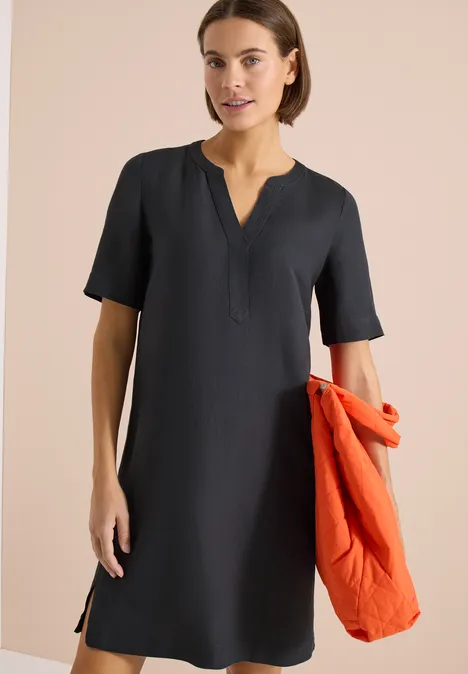 Donkerblauwe knielange jurk met V-hals en korte mouwen, vrouw met oranje jas.